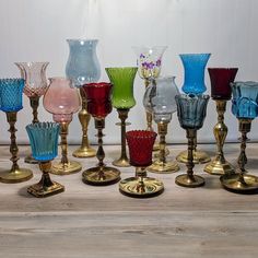 many different colored glass vases lined up on a table top with gold bases and feet