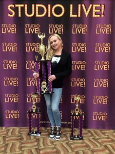 a woman standing next to two trophies in front of a purple backdrop with the words studio live on it