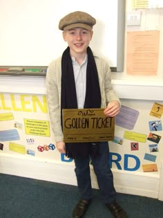 a young boy wearing a hat and scarf holding a sign that says golden ticket in front of him