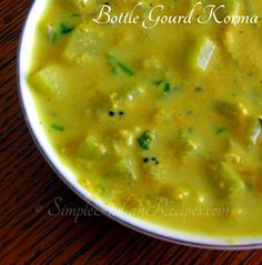 a white bowl filled with yellow soup on top of a wooden table next to a spoon