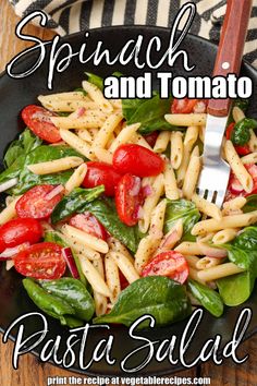 spinach and tomato pasta salad in a black bowl with a fork on the side