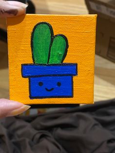 a person holding up a small piece of wood with a painting of a plant on it