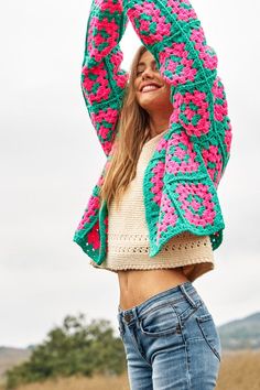 a woman is holding her arms up in the air while wearing a crocheted sweater