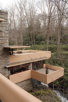 a house built into the side of a hill with trees in the foreground and water running through it