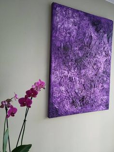 a purple painting hangs on the wall next to a vase with pink flowers in it