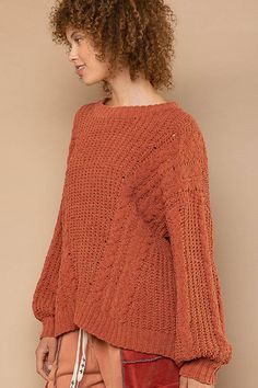 a woman with curly hair wearing an orange sweater and brown pants, looking off to the side