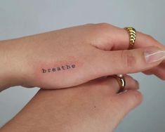 two hands holding each other with the word breathe tattooed on their wrist and one has a gold band