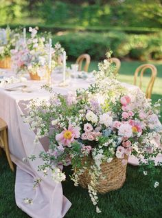 a table with flowers and candles on it in the middle of some grass, next to a wicker basket