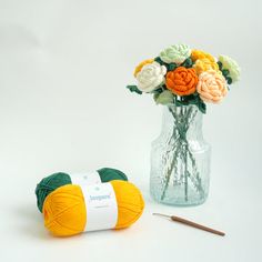 a vase filled with flowers next to a ball of yarn and a crochet hook