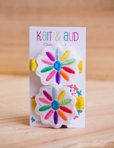 two colorful flower clips on a card with the words kalt & aud written below them