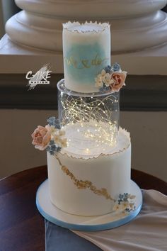 a three tiered wedding cake with flowers on the top and blue frosting is sitting on a table