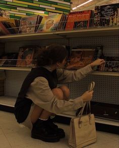 a woman kneeling down in front of a book shelf with a purse on her lap