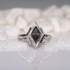 a white diamond ring sitting on top of a table next to some rocks and snow