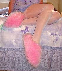 a woman sitting on top of a bed with pink fuzzy feet