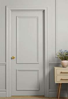 an empty room with a white door and some flowers on a small table next to it