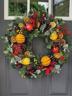 a christmas wreath with fruit and pine cones on the front door, hanging from a window