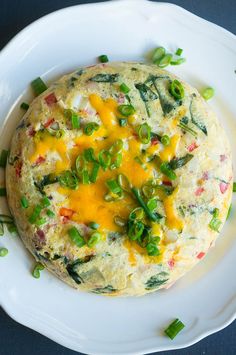 an omelet with green onions and cheese on a white plate next to peas