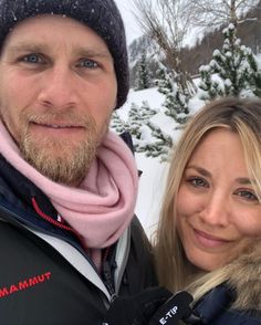 a man and woman standing in front of snow covered trees