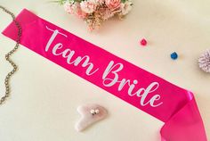 a pink sash with the word team bride on it next to some flowers and beads