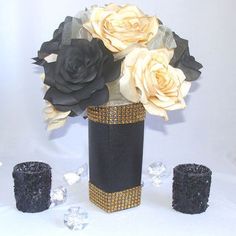 a black vase with flowers and candles on a white tableclothed cloth, surrounded by crystal stones