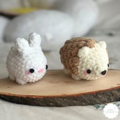 two small crocheted animals sitting on top of a wooden slice