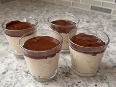 four glasses filled with dessert sitting on top of a counter