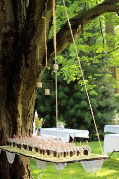 an outdoor wedding setup under a tree with mason jars on the table and hanging from a rope