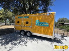 a yellow trailer parked on the side of a road next to a tree and fence