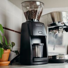 a black coffee maker sitting on top of a counter next to a potted plant