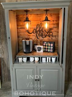 a small coffee bar with two lights on top and some cups in the bottom drawer