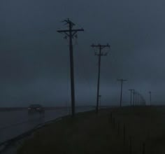 a car driving down the road on a rainy night with power lines and telephone poles