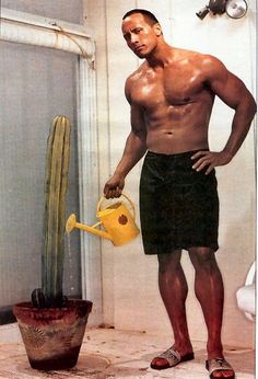 a man with no shirt holding a watering can next to a cactus