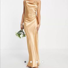 a woman in a gold dress holding a bouquet and standing next to a white wall