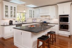 a large kitchen with white cabinets and black counter tops, an island in the middle