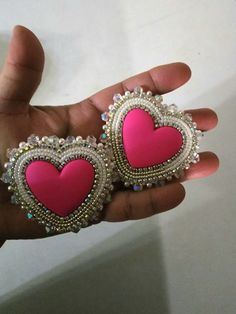 two pink heart shaped earrings are held in someone's hand