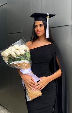 a woman wearing a graduation cap and gown holding a bouquet of flowers in her hands