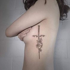 a cross tattoo on the back of a woman's left arm and shoulder, with flowers around it