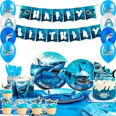 a birthday party set up with blue decorations and shark balloons, cupcakes and plates