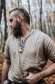 a man with a long beard wearing a necklace in the middle of a wooded area