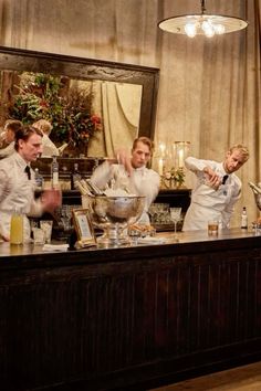 three people in white uniforms are preparing food at a bar with two women and one man