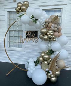 the balloon arch is decorated with gold and white balloons, greenery, and leaves