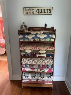 a wooden shelf filled with lots of quilts on top of a hard wood floor