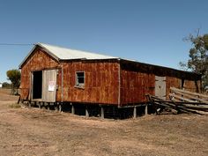 an old wooden building in the middle of a dry grass field next to a fence