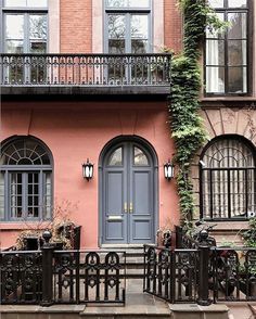 a pink building with black wrought iron railings and blue front door surrounded by greenery