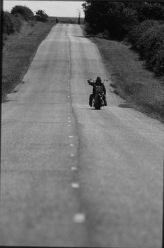 a person riding a motorcycle down the middle of an empty road in black and white