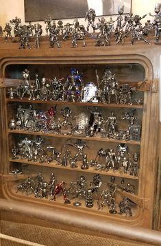 a display case filled with metal figurines on top of wooden shelves next to a painting