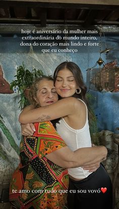 two women hugging each other in front of a wall with words written on the side