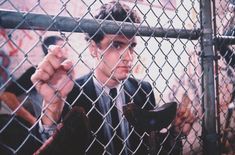 a man in a suit and tie behind a chain link fence holding his fist up