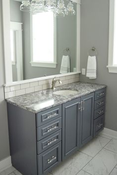 a bathroom with gray cabinets and marble counter tops