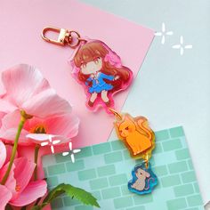 two keychains with cartoon characters on them next to flowers and a pink flower